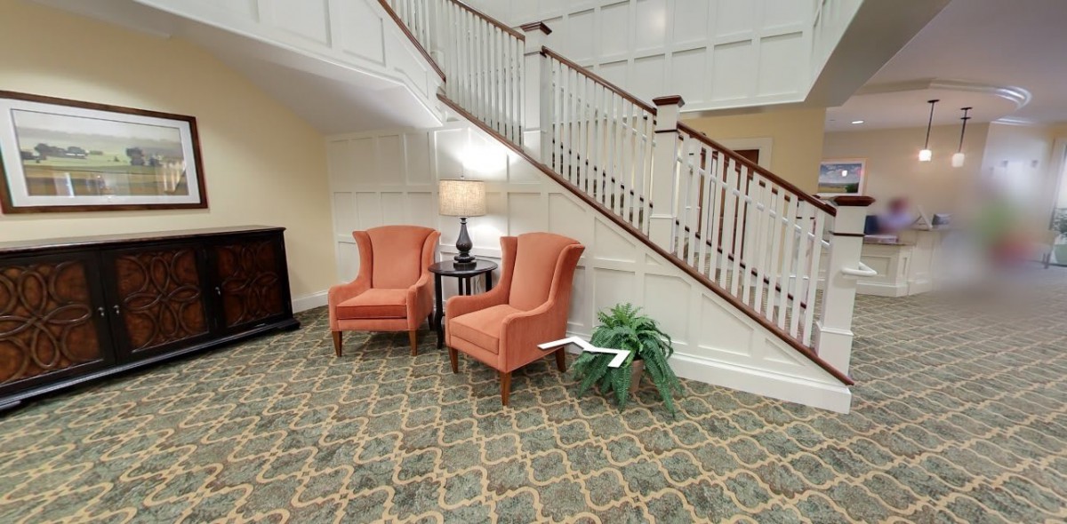 A cozy seating area with two orange armchairs and a lamp near a staircase.