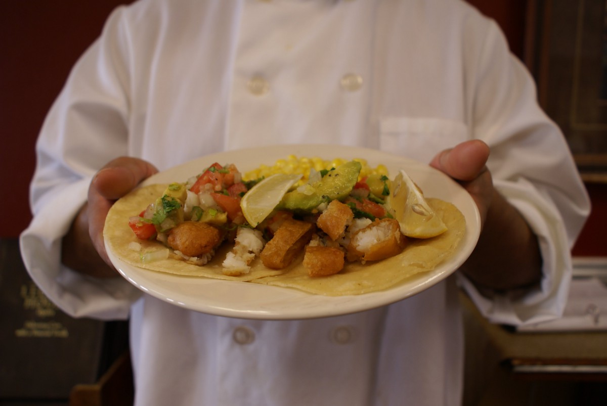 A chef presenting a plate of delicious tacos topped with fresh ingredients.