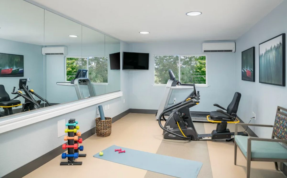 A small gym room with exercise equipment including a treadmill, stationary bike, dumbbells, and a yoga mat.