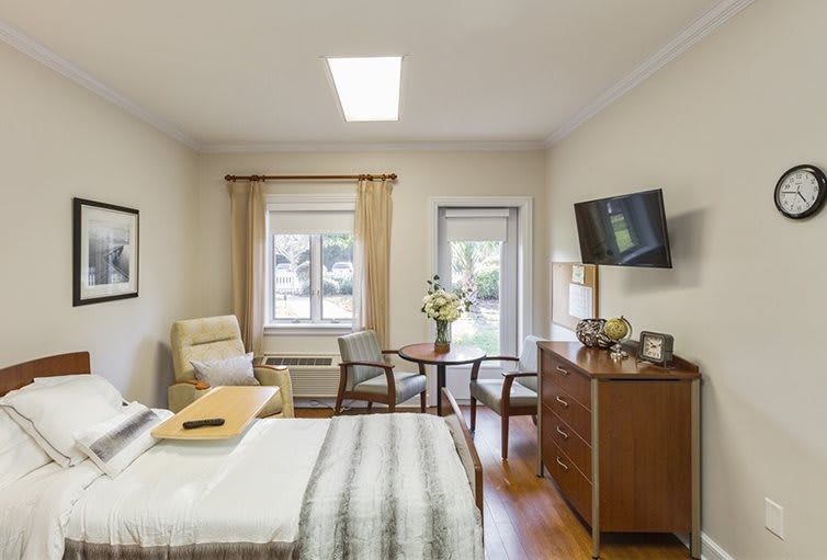 A cozy and modern bedroom featuring a comfortable bed, seating area, TV, and large window allowing ample natural light.