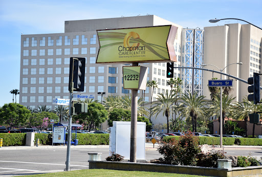 A brightly colored restaurant sign in an urban setting, surrounded by palm trees and modern buildings.