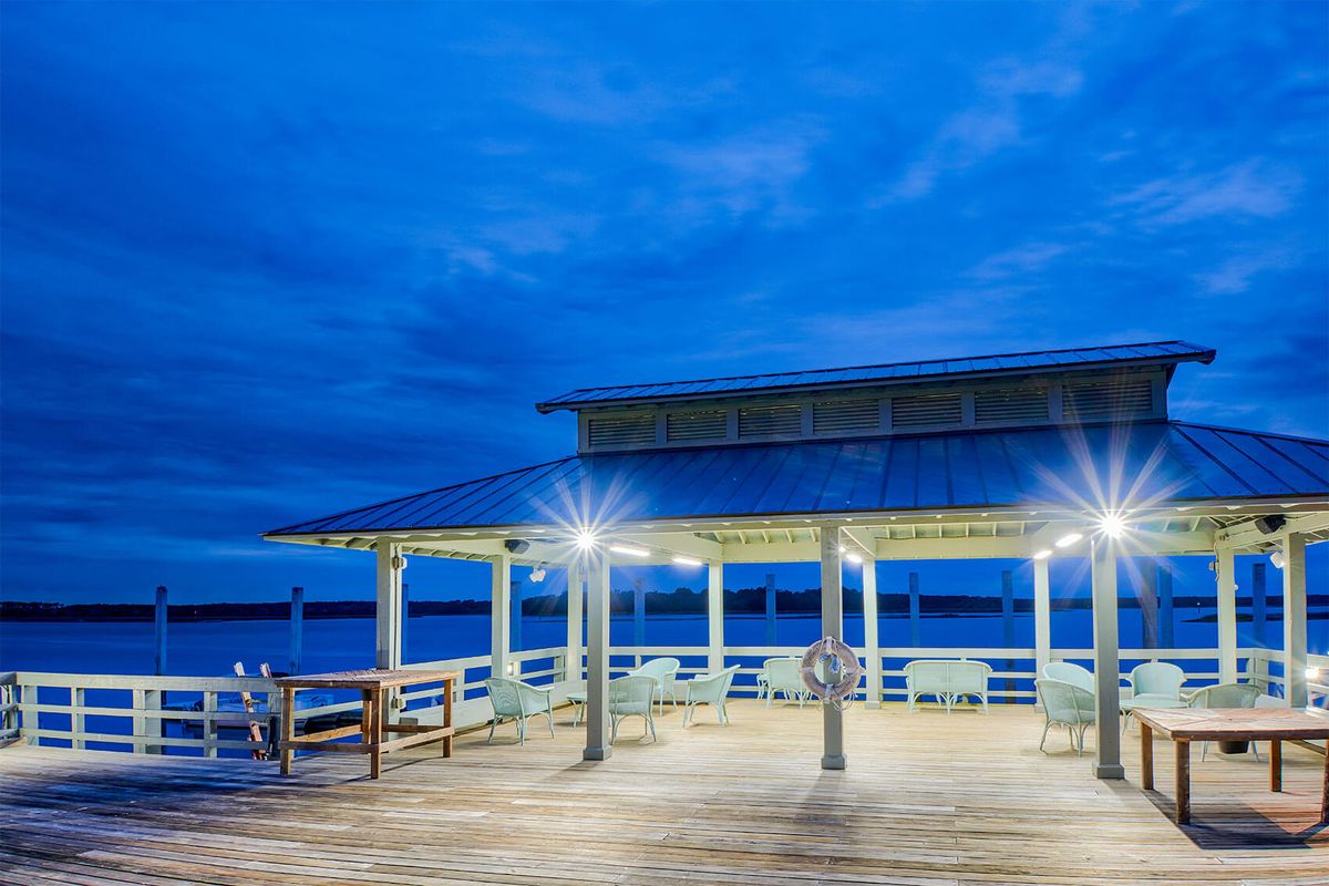 A lit pier with a gazebo at dusk under a cloudy sky.