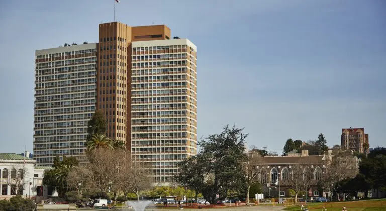A tall, modern building surrounded by greenery under a clear sky.
