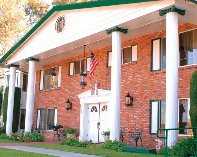 A two-story brick house with prominent white columns and an American flag displayed at the entrance.