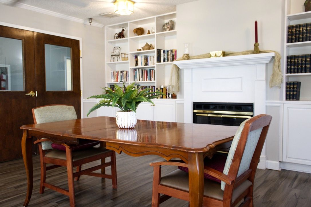 A cozy dining room with a wooden table, chairs, and an indoor plant, complemented by a white fireplace and built-in bookshelf.