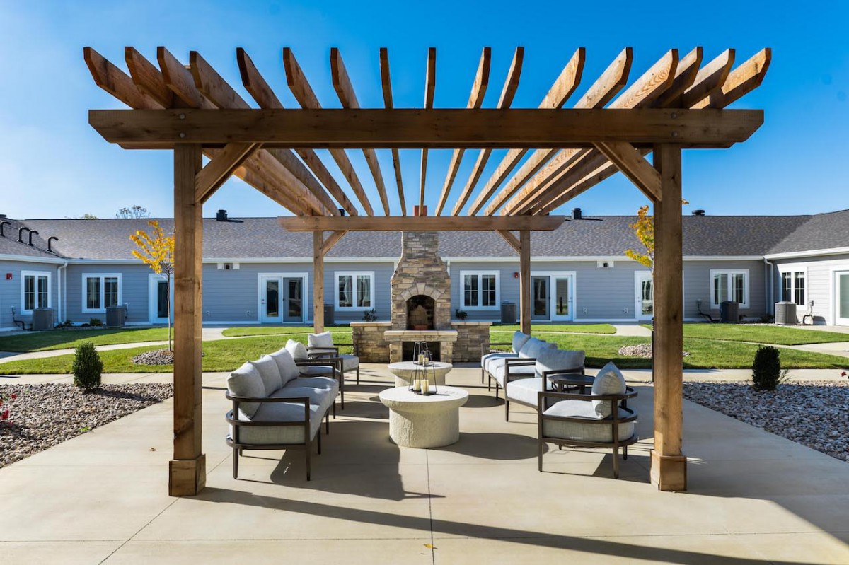 A beautifully designed outdoor patio area with a pergola, comfortable seating, and a central fireplace.