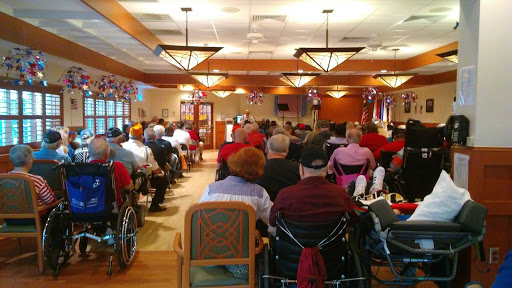 A gathering of senior citizens in a community center, seated and attentive during an event.