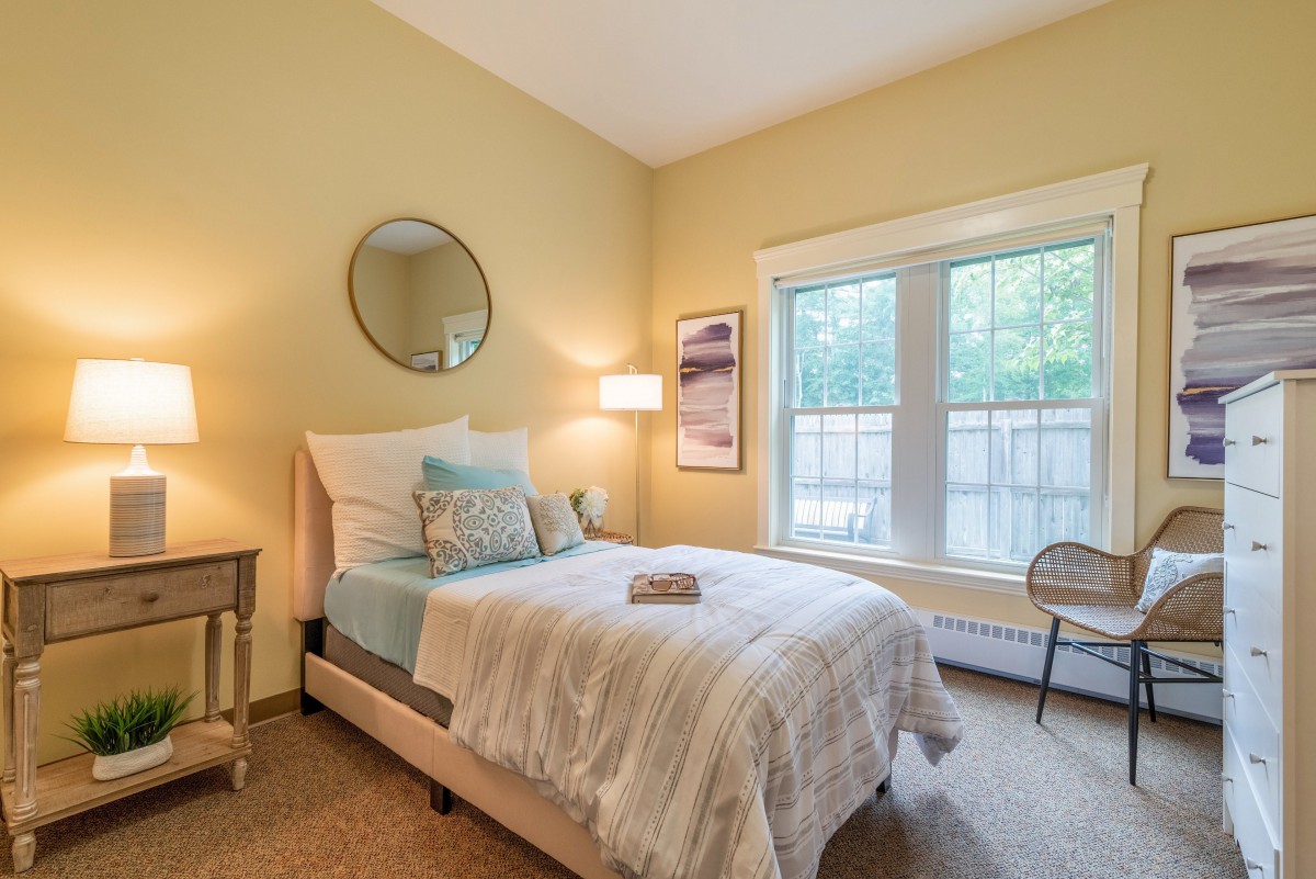 A cozy bedroom with a neatly made bed, soft lighting, and a large window.