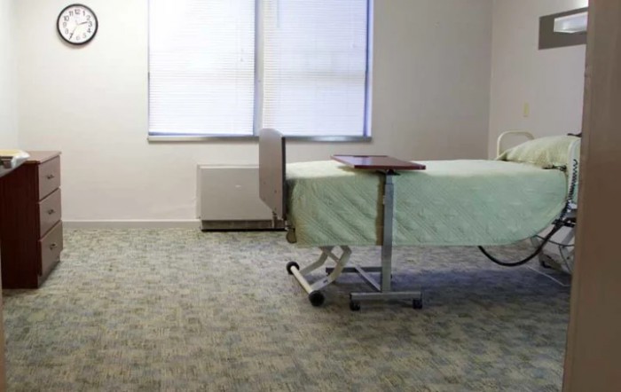 A hospital room with a single bed and an adjustable table by the window.