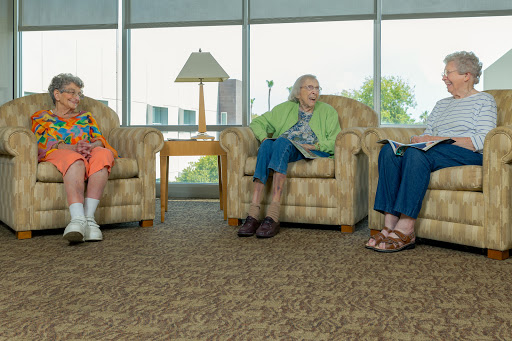 A relaxed gathering of three elderly women conversing in a comfortable lounge area.