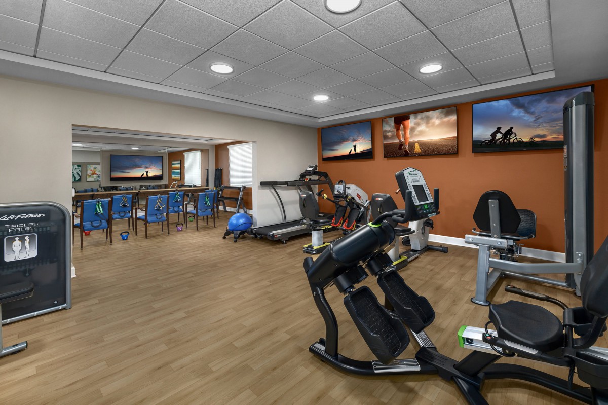 A modern gym with various fitness equipment and a wooden floor.