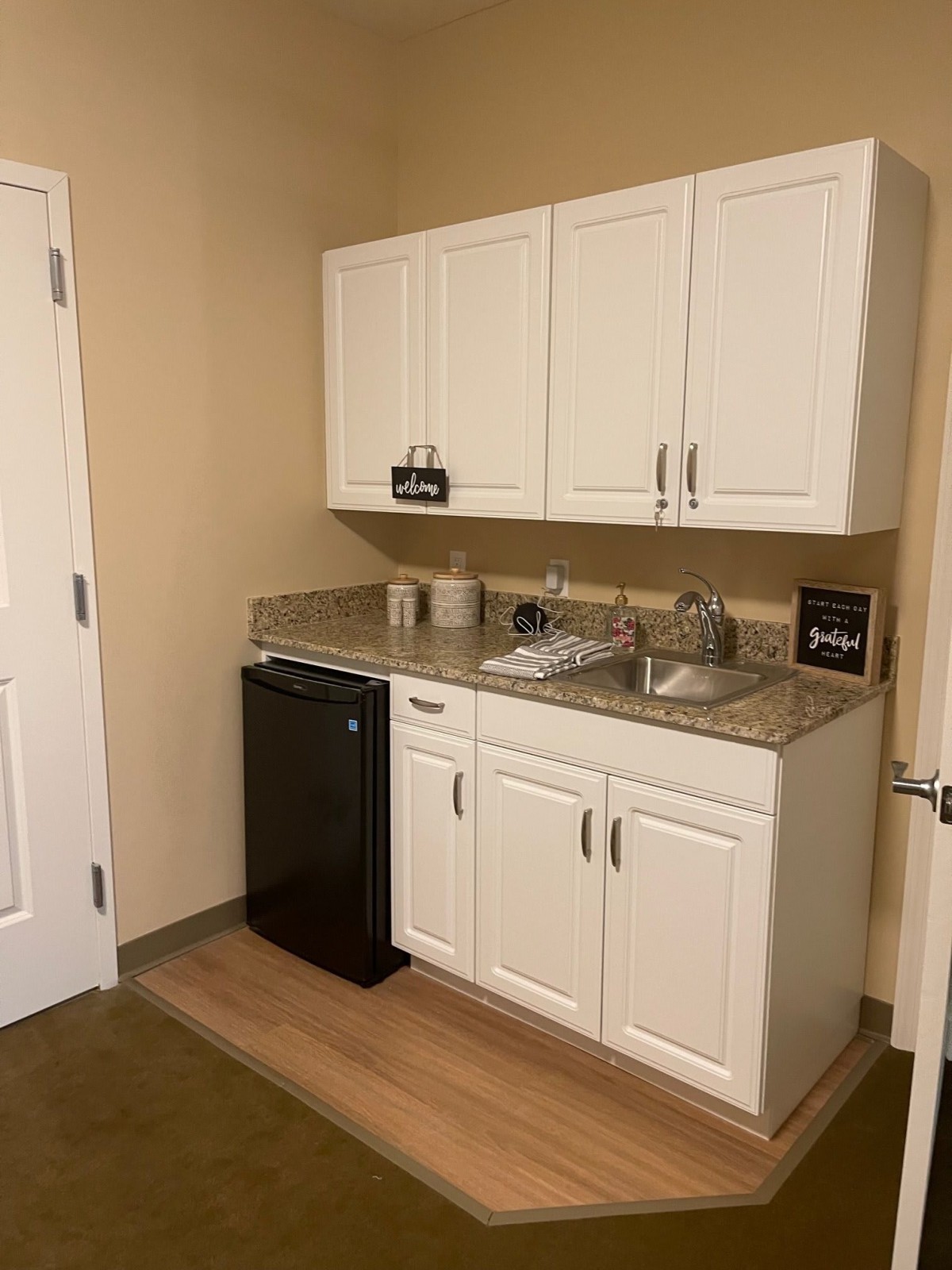 Compact kitchenette with white cabinets and a mini fridge.