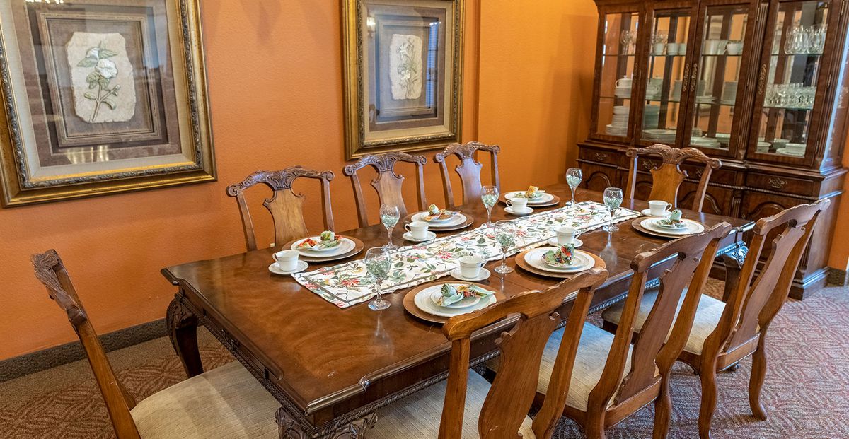 A dining room features a wooden table set elegantly with glassware and decorative ceramic plates, complemented by a patterned table runner.