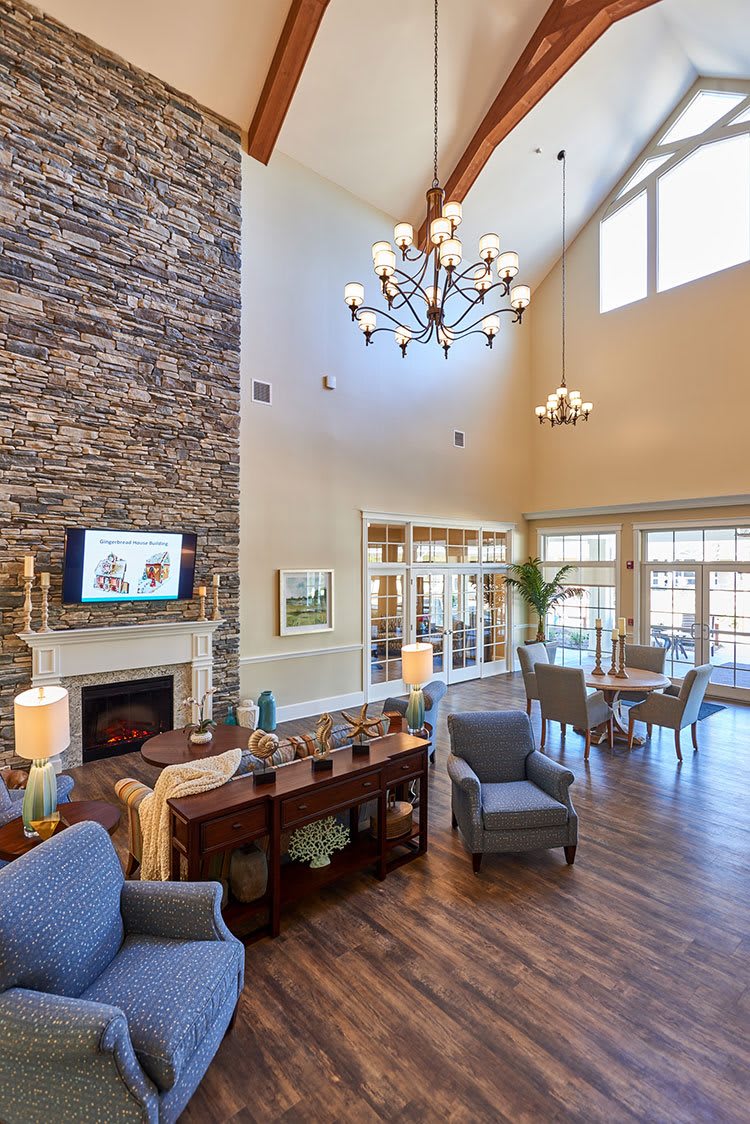 A spacious and elegantly decorated living room with a high ceiling, large windows, a stone fireplace, and stylish furniture.