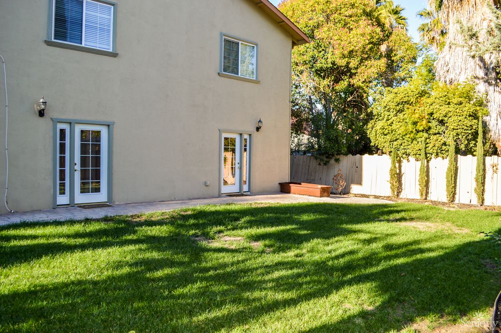A sunny backyard with a well-maintained lawn, bordered by trees and a wooden fence.
