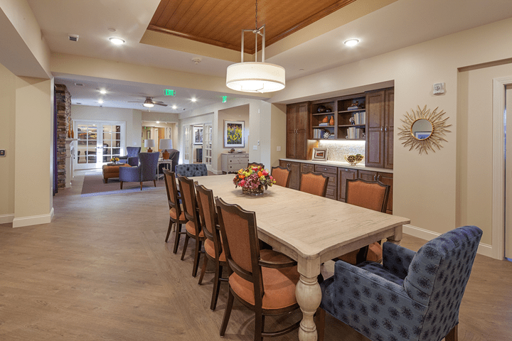 A modern dining room with a large table and stylish chairs, featuring warm lighting and wooden accents.