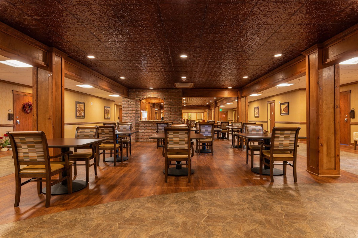 A warmly lit restaurant interior with wooden floors and empty tables.