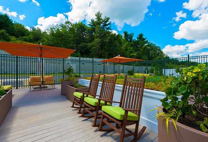 A rooftop garden with wooden rocking chairs and orange umbrellas under a bright blue sky.