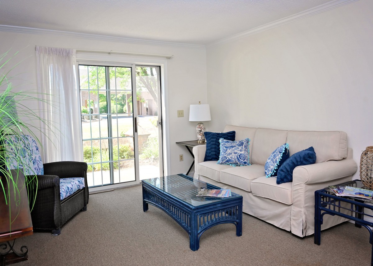 A cozy living room with a beige couch, blue coffee table, and sliding glass door.