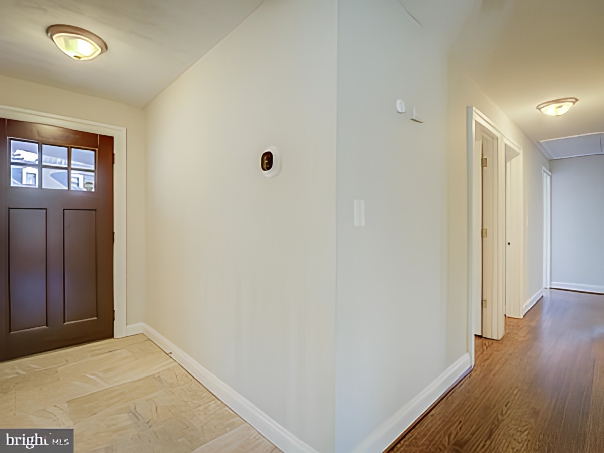 A well-lit hallway with wooden flooring and a brown door.