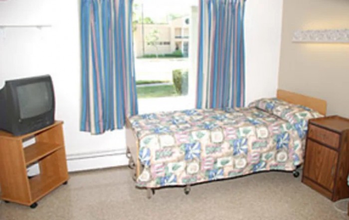 A modest room featuring a single bed with colorful bedding, positioned next to a window with blue striped curtains.