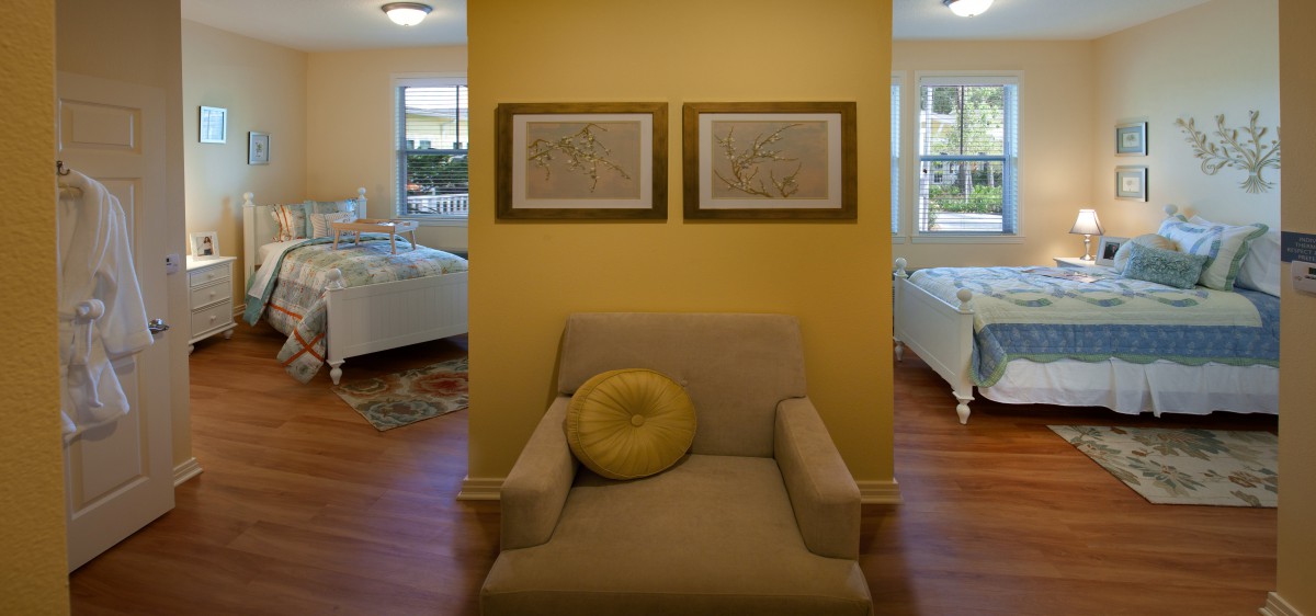 A cozy armchair with a decorative cushion sits against a yellow wall, adorned with framed artwork.