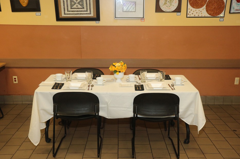 A neatly set dining table in a restaurant with white tablecloth and yellow flowers.