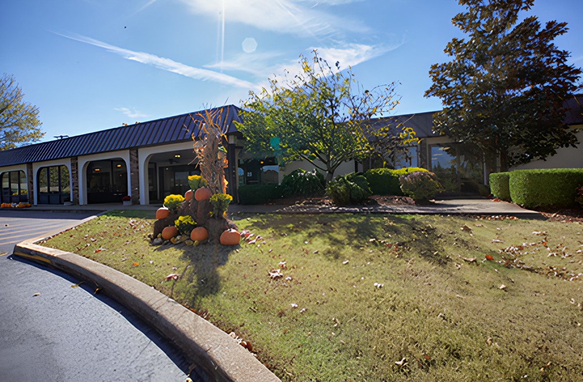 A sunny day view of a building with surrounding trees and flowers.