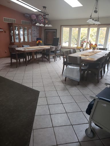 A spacious dining room with large tables and numerous chairs, well-lit by natural light through the windows.