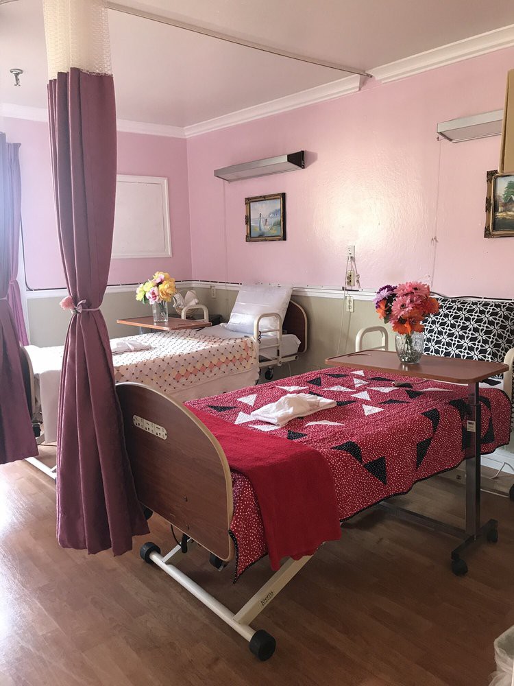 A shared hospital room with two beds, chairs, and decorative flowers.