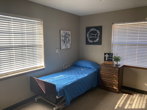 A cozy room featuring a hospital bed with a blue blanket, surrounded by natural light from the windows.