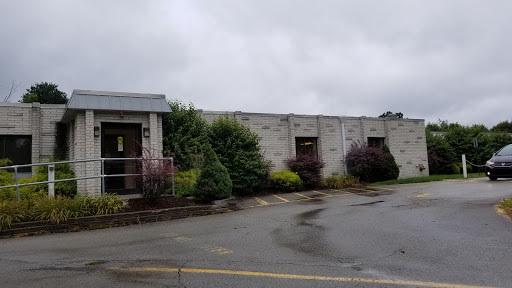 A weathered building surrounded by overgrown foliage on a rainy day.