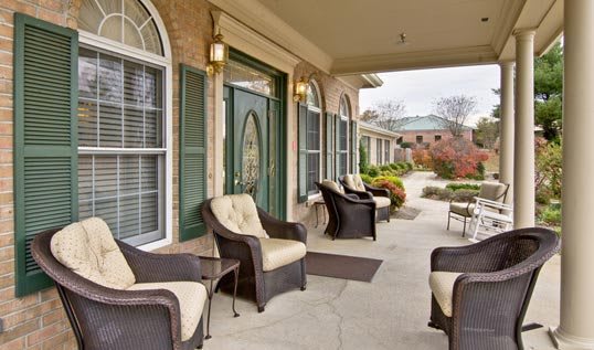 A cozy porch with wicker chairs and decorative windows, leading to the entrance of a building.