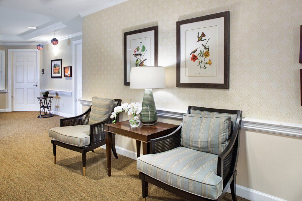 A cozy sitting area with two upholstered chairs, a table, and framed artwork on the wall.