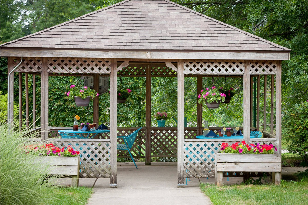A charming wooden gazebo adorned with vibrant hanging flower baskets and surrounded by lush greenery.
