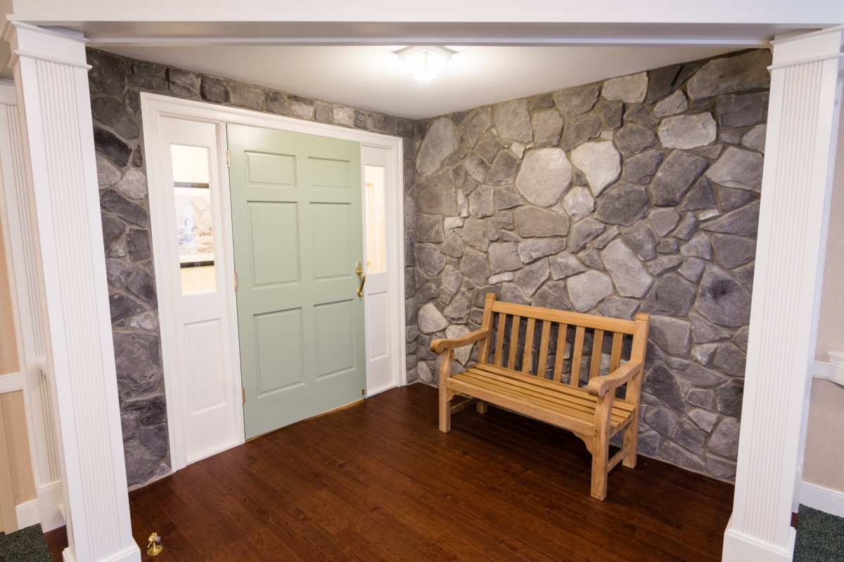 An interior space featuring a stone accent wall, wooden bench, and a light green door.