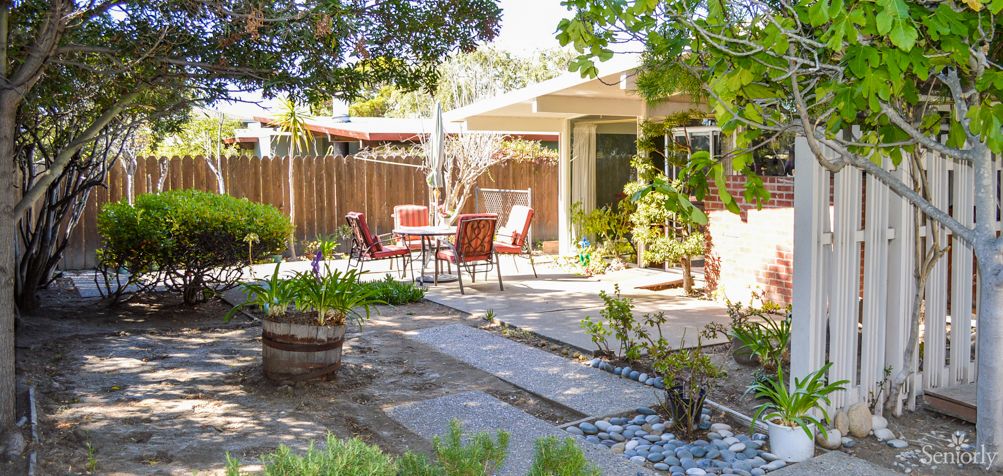A serene backyard patio with outdoor furniture, surrounded by lush plants and a sunny atmosphere.