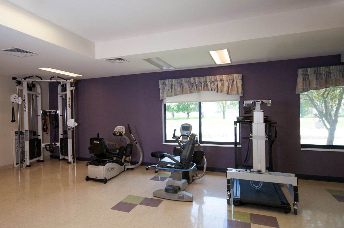 A gym room featuring various exercise equipment and a purple accent wall.