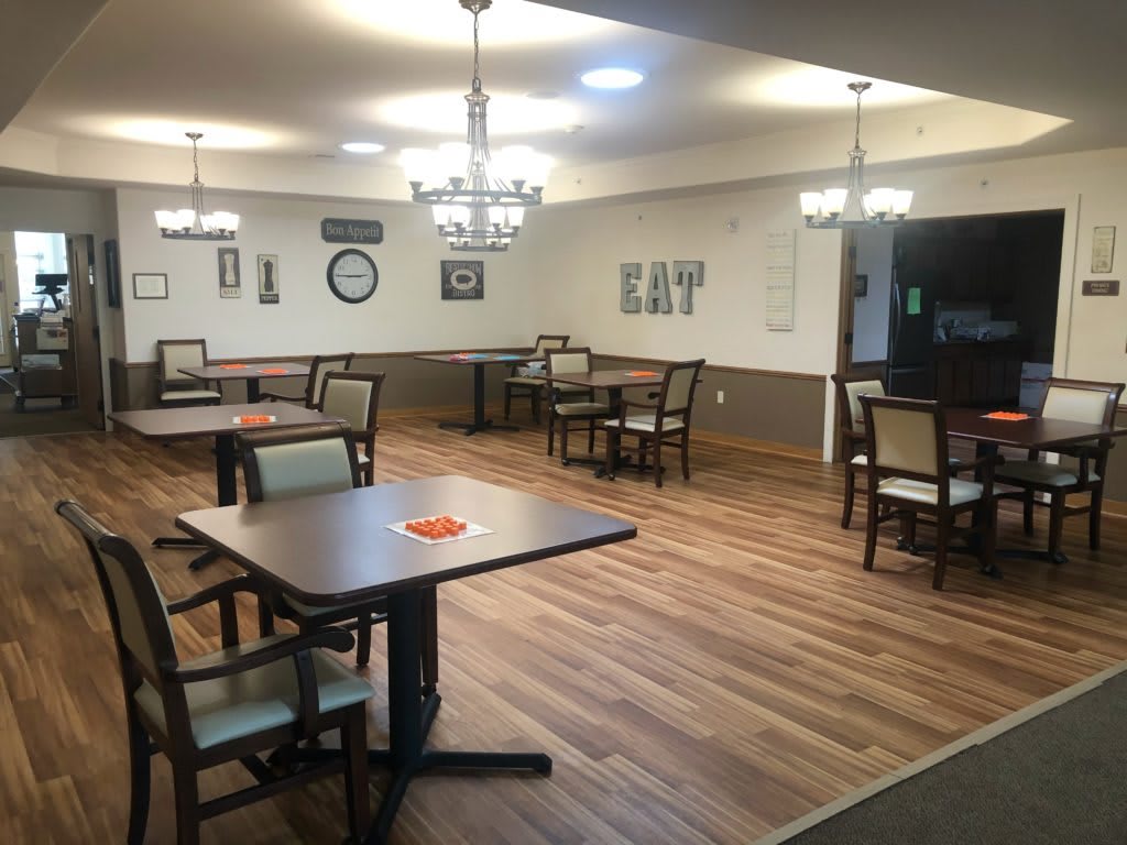 A well-lit dining area with neatly arranged tables and chairs, featuring chandeliers and wooden flooring.