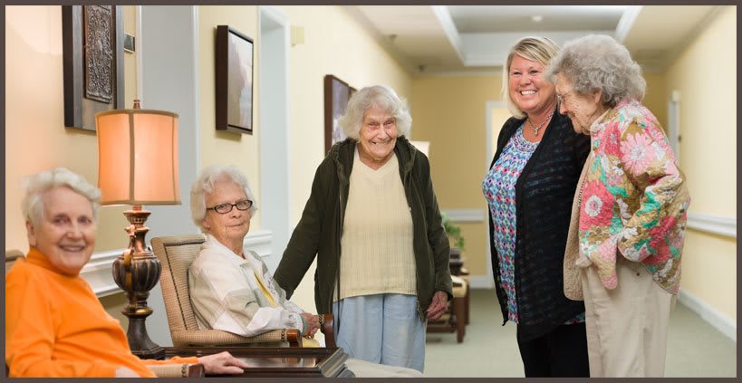 A group of elderly women and a caregiver in a nursing home setting.