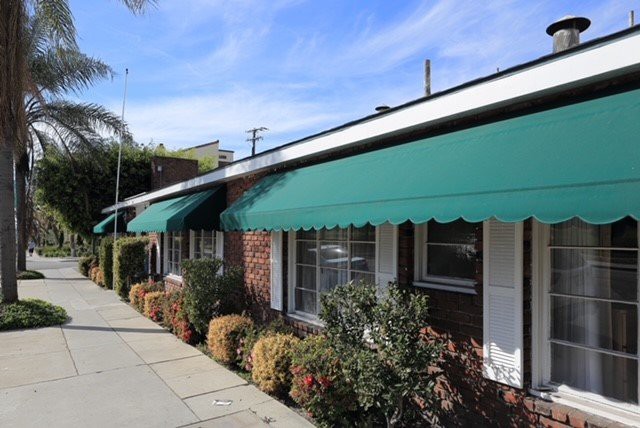 A brick building with green awnings lining a sunny sidewalk.
