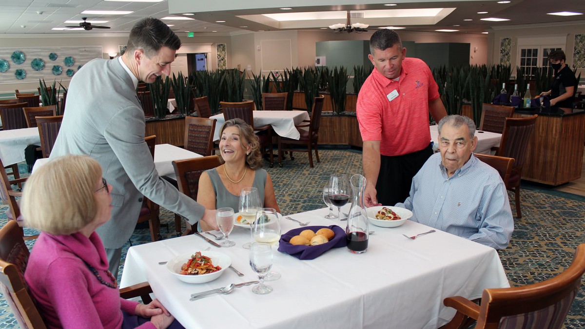 A group of people enjoying a meal at a restaurant with servers attending to them.