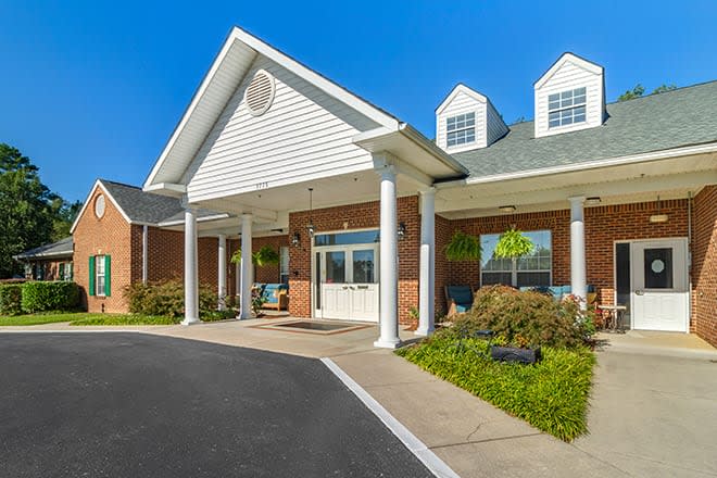 A sunny day view of a building entrance with columns and landscaping.