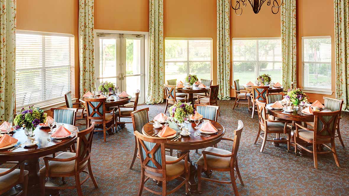 A well-decorated dining room featuring round tables with elegant place settings and large windows providing natural light.