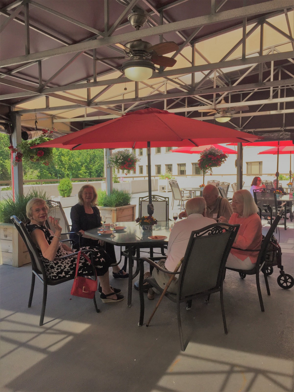 A group of people enjoying a meal together on a shaded patio with red umbrellas.