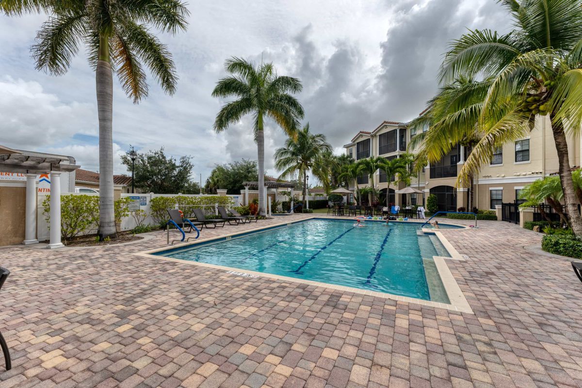 A serene outdoor swimming pool surrounded by palm trees and residential buildings under a cloudy sky.