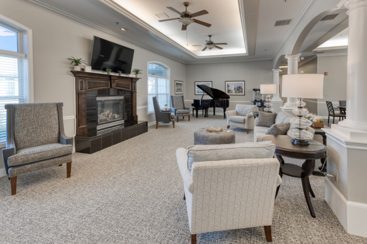 A spacious and elegantly decorated living room featuring a grand piano, comfortable seating, a fireplace, and a large TV.