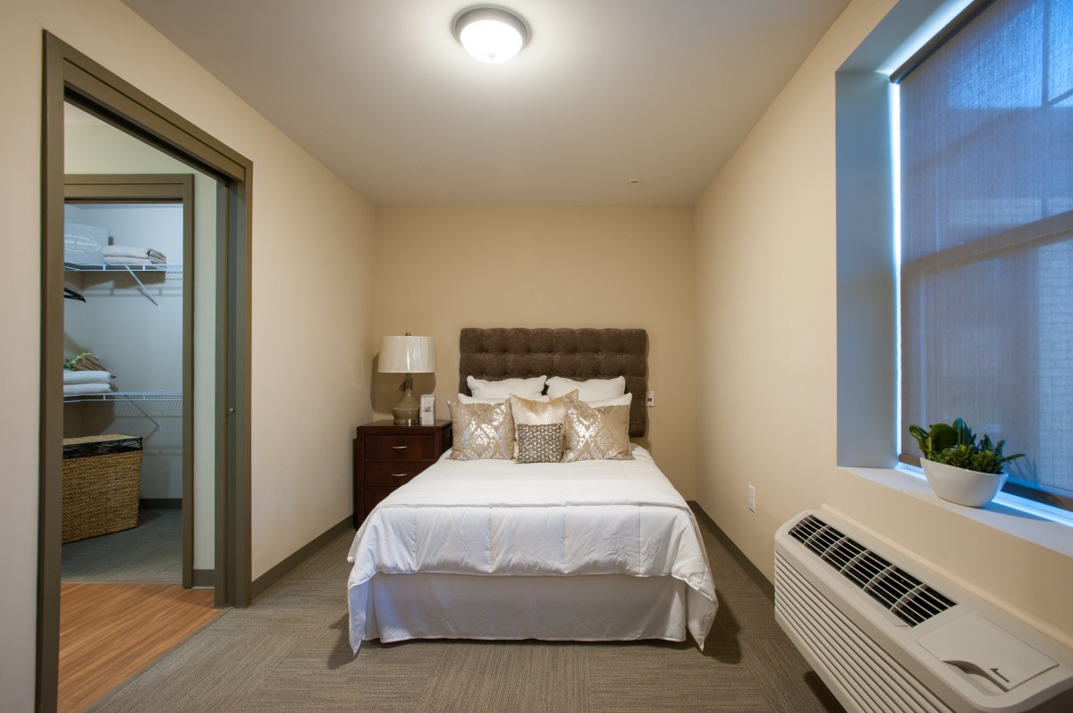 A cozy bedroom with a neatly made bed, bedside table, and a window.