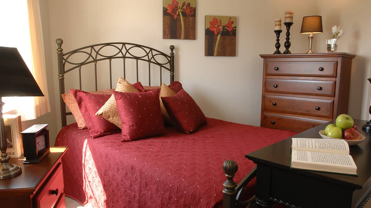 A cozy bedroom with red bedding and floral artwork on the wall.