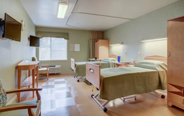 A clean and well-organized hospital room with two beds and a large window.